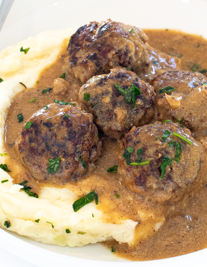 Swedish meatballs over mashed potatoes on a white plate.