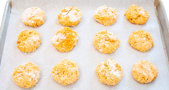 Raw biscuits lined up on a baking sheet with parchment paper on it. 