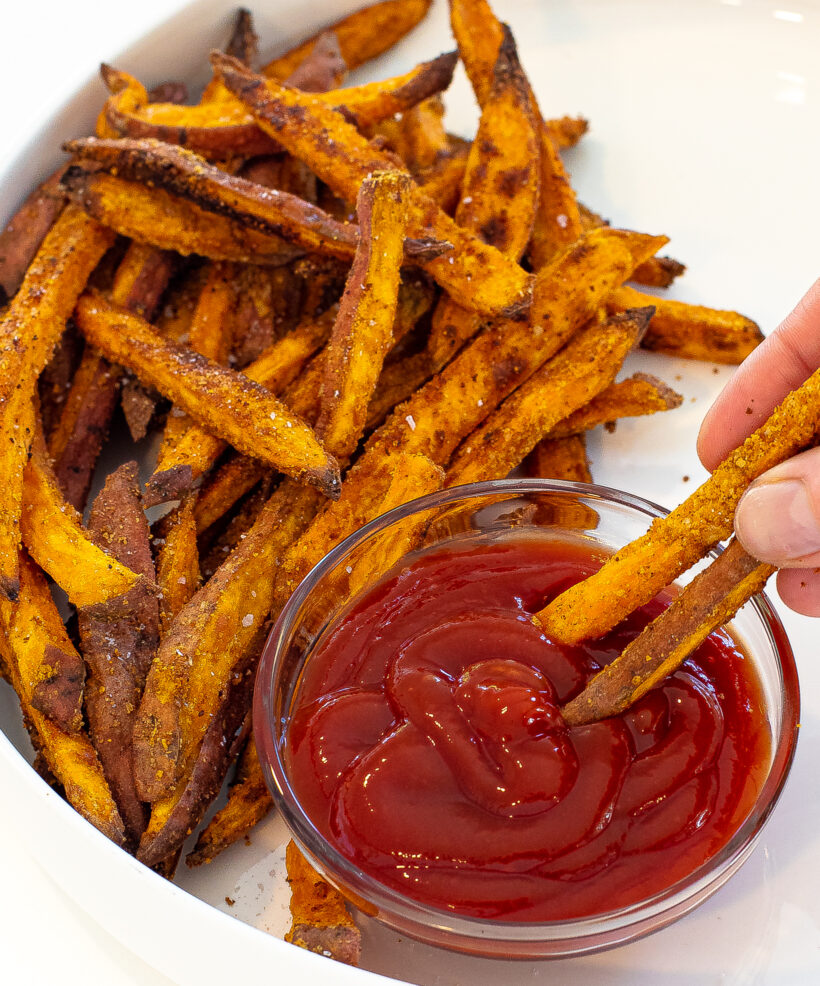 Hand with two fries in it dipping them into ketchup.