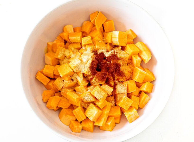 Cubed sweet potatoes in a mixing bowl with spices before combining.
