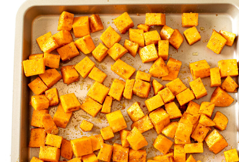 Sweet potatoes spread out on a sheet pan before going into the oven.