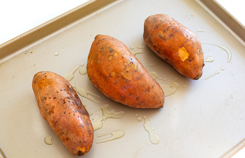 Three sweet potatoes on a sheet pan before being baked.