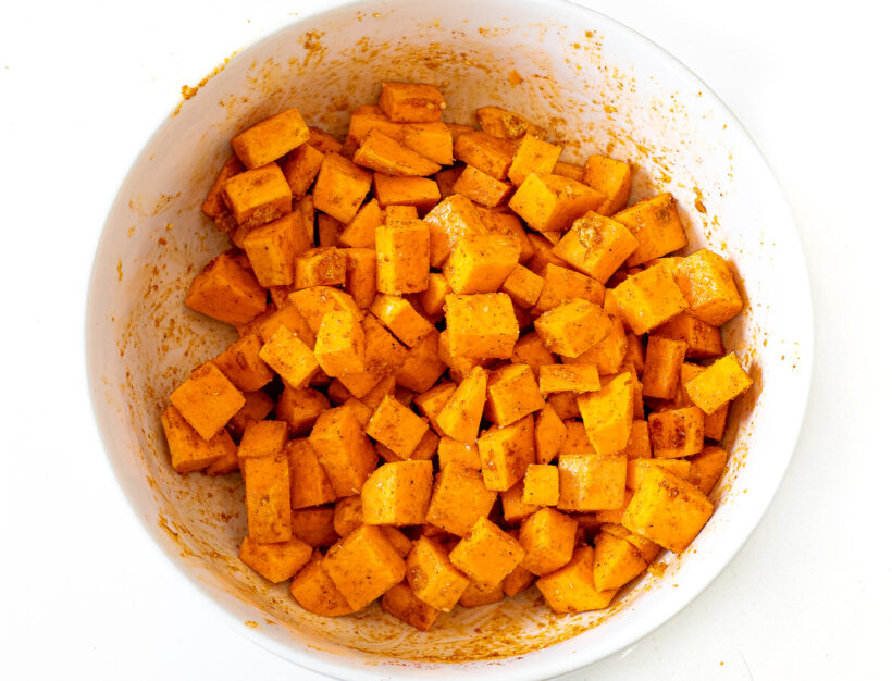 Cubed sweet potato pieces coated in spices in a mixing bowl.