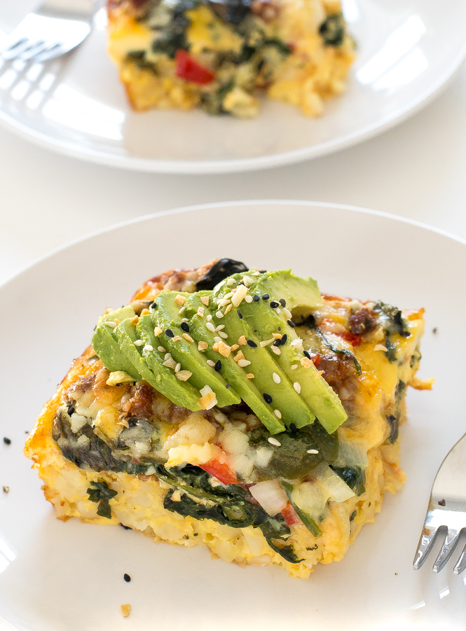 slice of breakfast casserole topped with sliced avocado on white plate