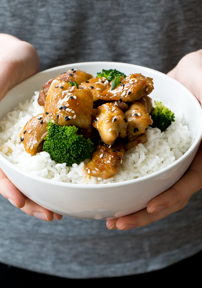 Hands holding white bowl with chicken, broccoli, and white rice