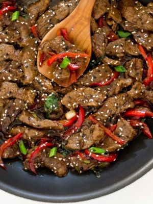 thai basil beef in pan with spoon and sesame seeds