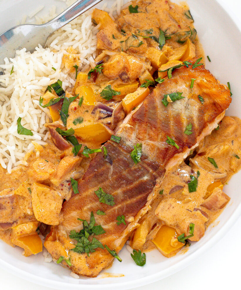 Coconut curry salmon on a bed of rice in a white bowl.