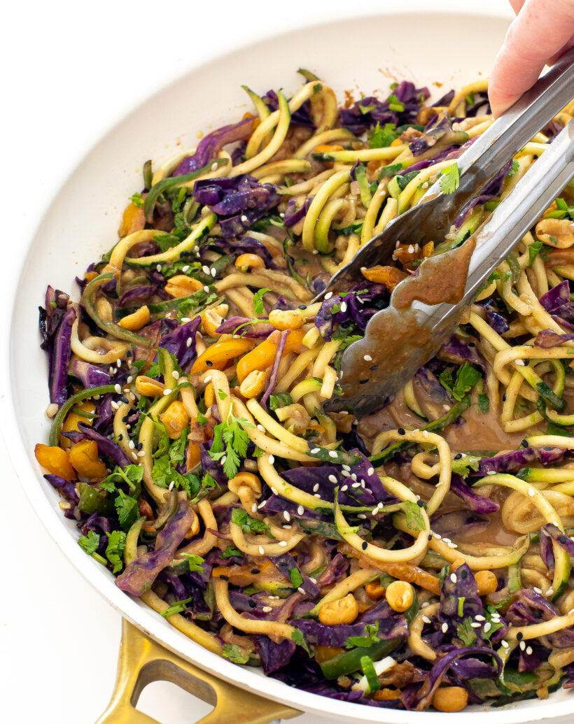 zucchini peanut noodles on a serving tray with silver tongs. 