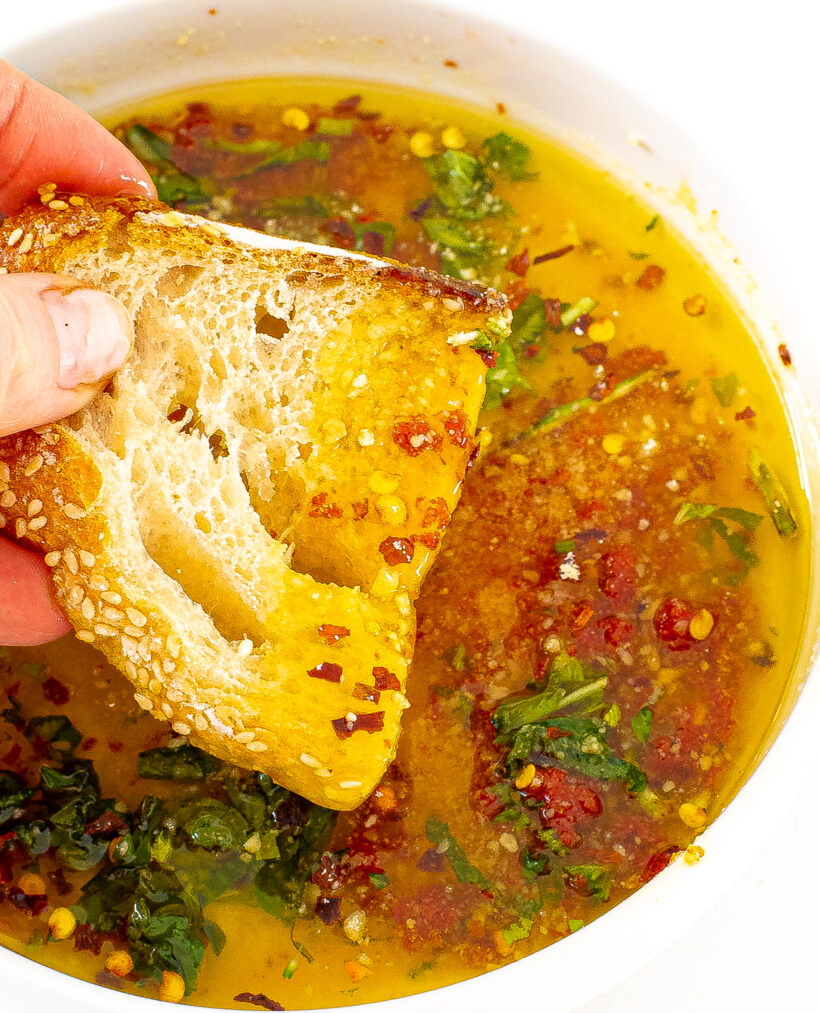 A hand dipping a piece of bread into the bowl of dipping oil.