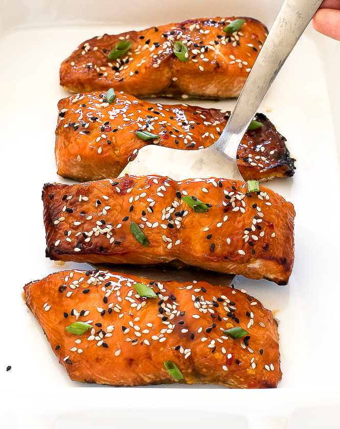 Sweet and Sour Salmon in a white casserole dish with a spatula lifting a piece of salmon.