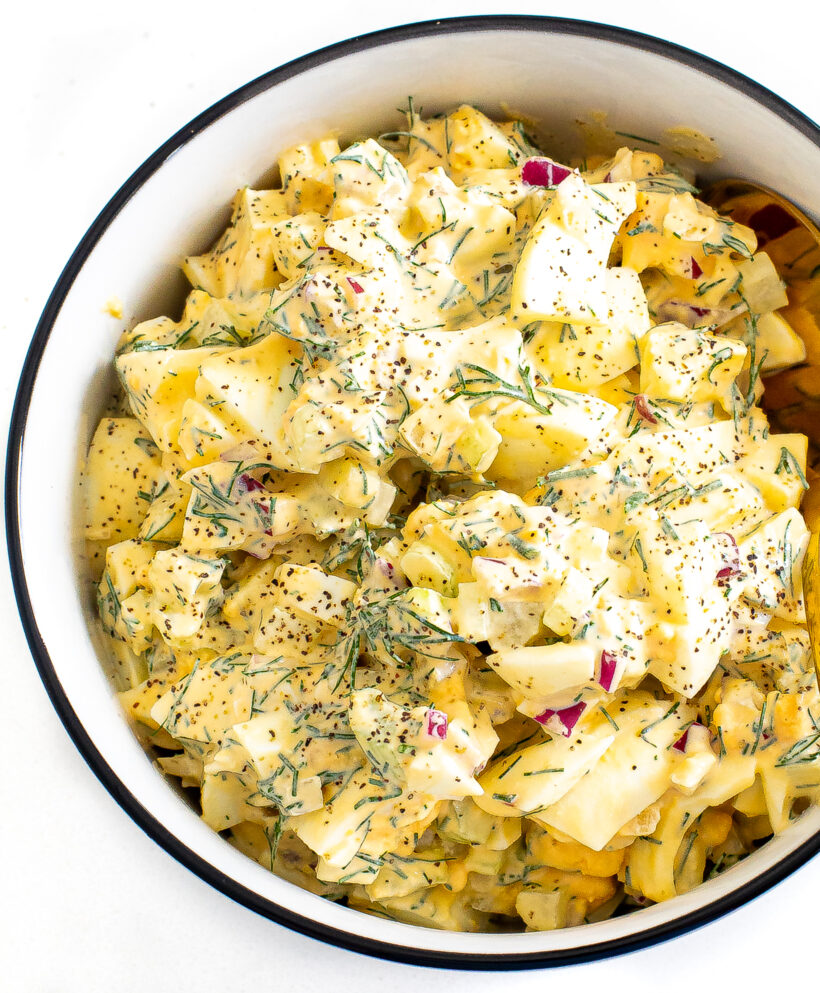 Egg salad in a bowl topped with fresh dill and pepper.