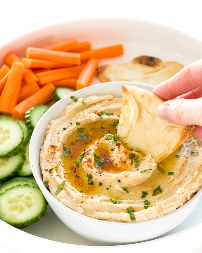 Person dipping pita bread into bowl of homemade garlic hummus.
