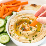 Person dipping baby carrot into bowl of hummus.