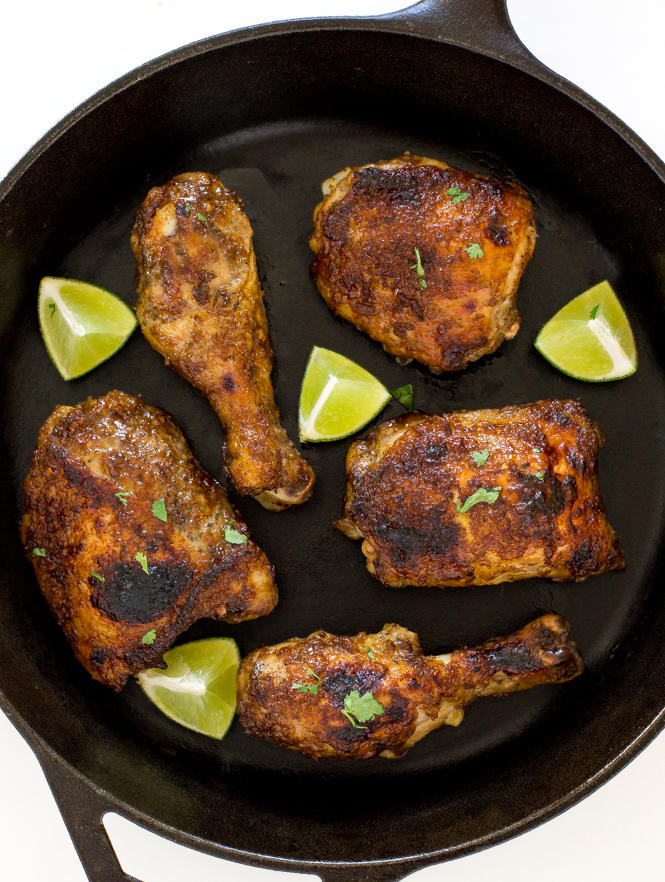 Baked jerk chicken in a skillet with lime wedges.