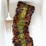 a white casserole dish with this sliced grilled skirt steak and chimichurri sauce poured over it with a large serving fork to the left | chefsavvy.com