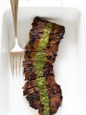 a white casserole dish with this sliced grilled skirt steak and chimichurri sauce poured over it with a large serving fork to the left | chefsavvy.com