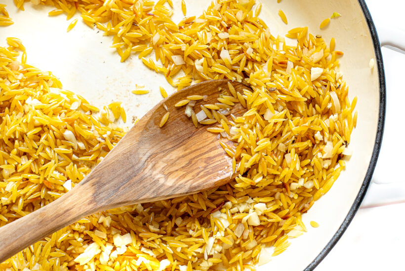 Toasted orzo in a white skillet.