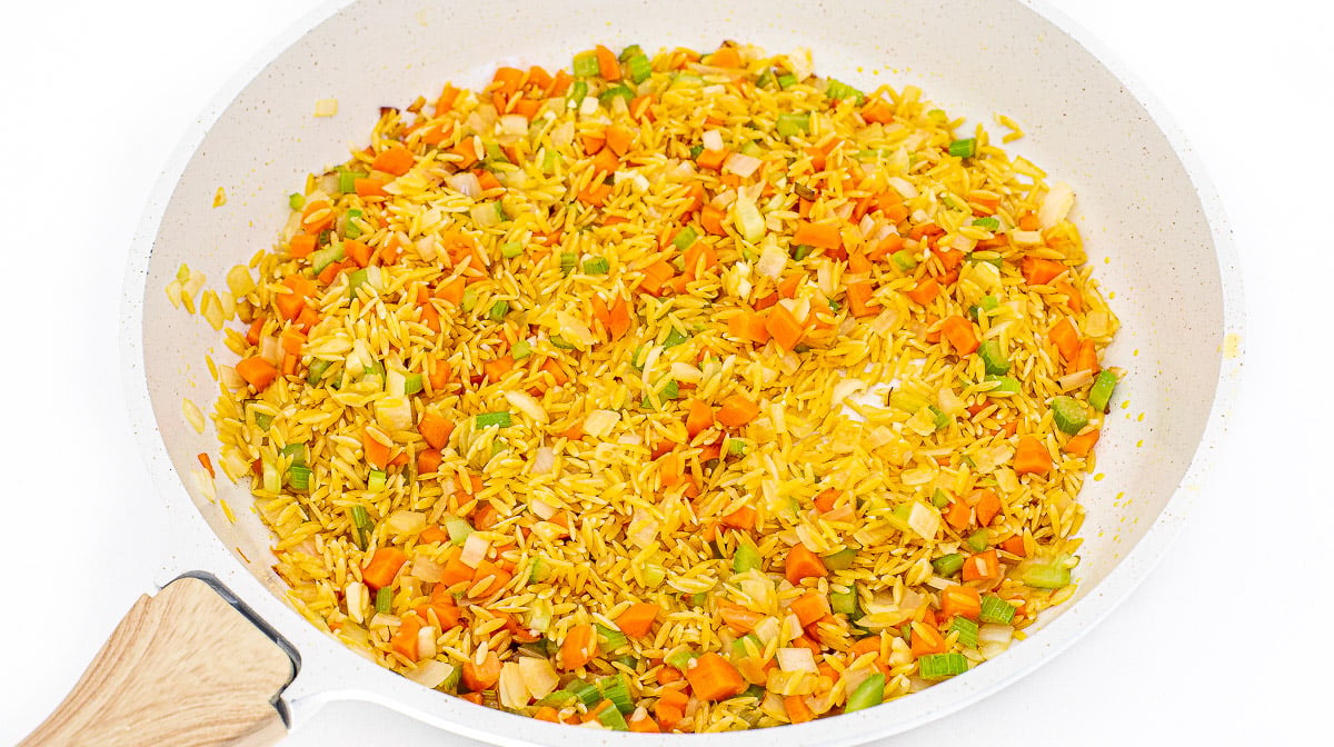 Toasting orzo with veggies in a skillet.