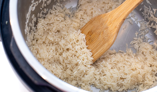 Uncooked rice being sautéed in an instant pot with a wooden spoon.