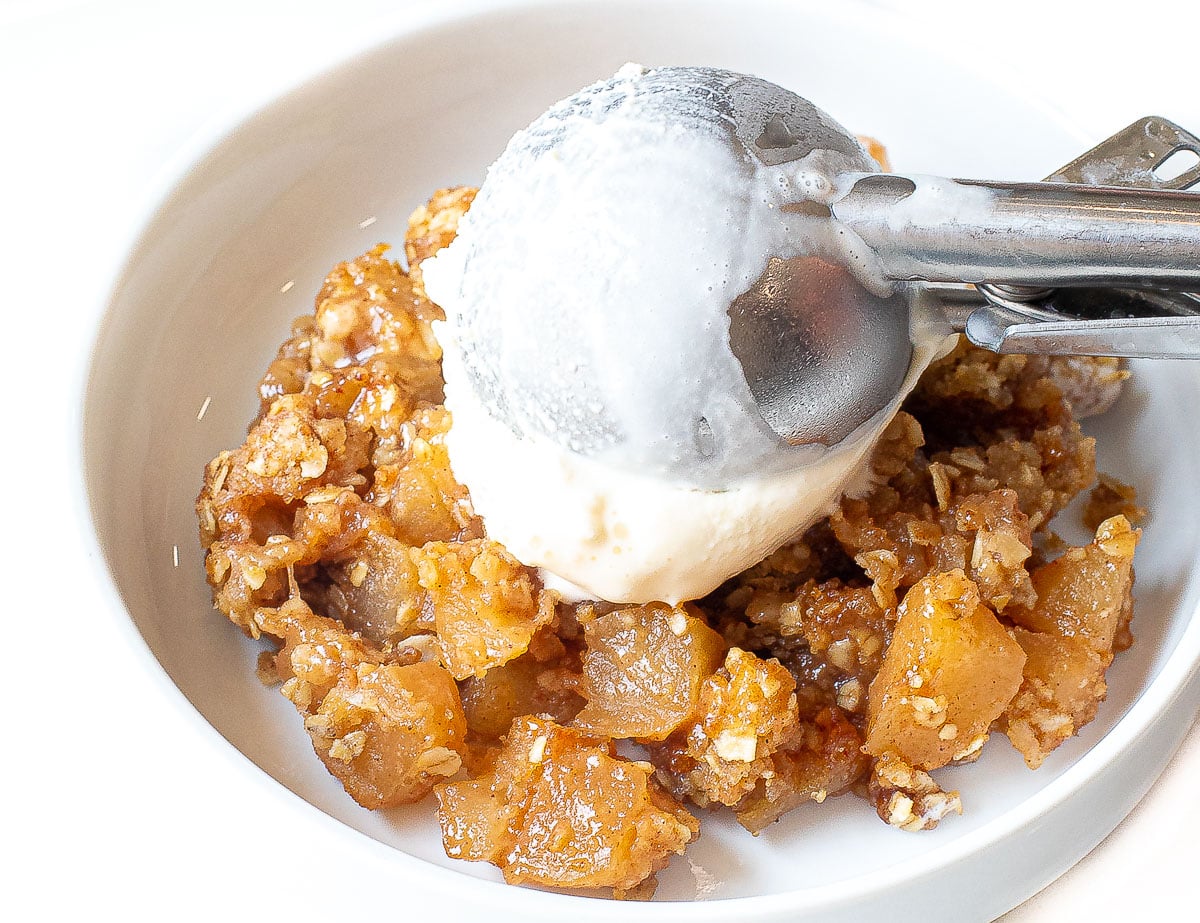 Adding a scoop of vanilla ice cream over an apple crisp in a bowl.