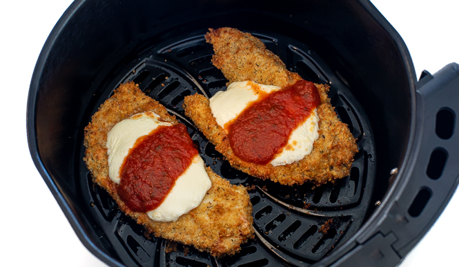 Two chicken parmesan cutlets in the air fryer topped with cheese and tomato sauce. 