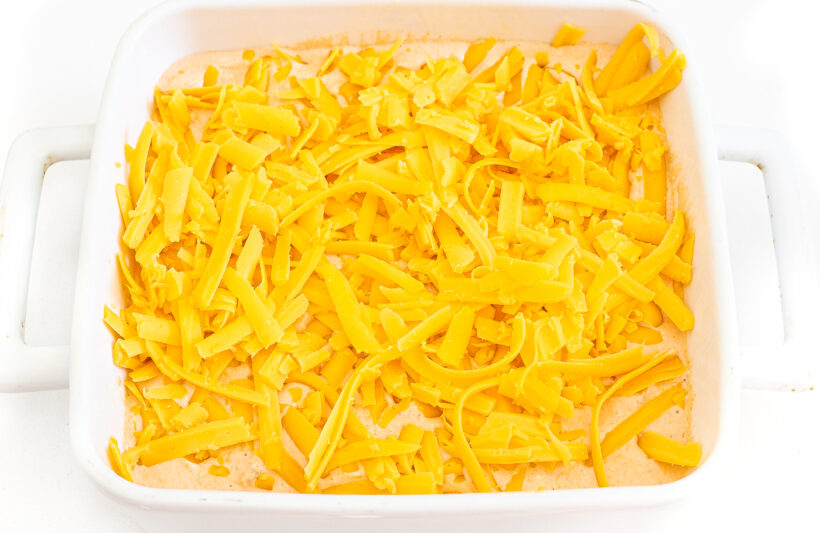 Shredded cheddar cheese spread on top of the dip in a baking dish.