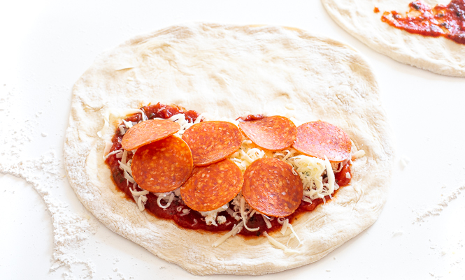topping calzones with mozzarella cheese, pepperonis and tomato sauce