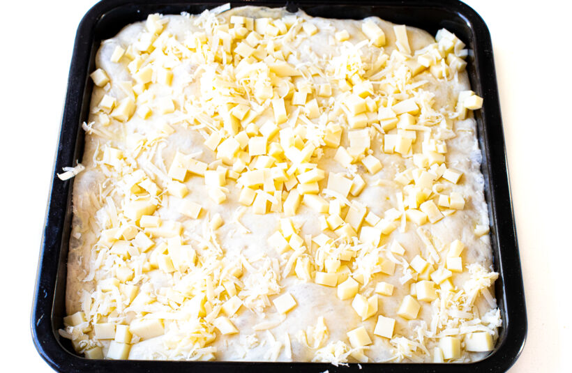 Pizza dough topped with cubes of mozzarella cheese.