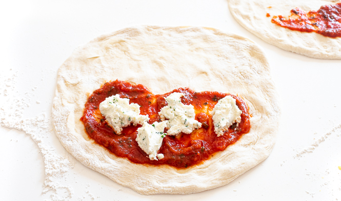 Dough rolled out to a circle with one half with tomato sauce and ricotta on it.
