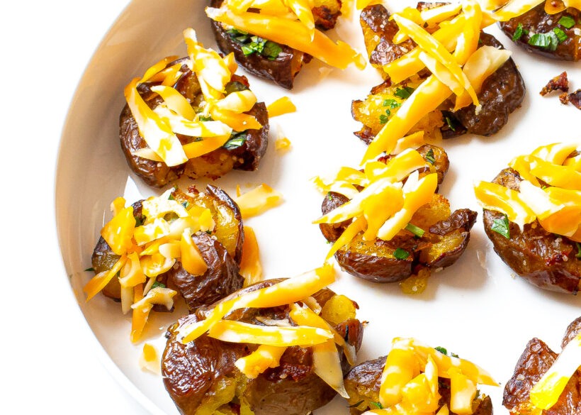 Smashed potatoes on a plate sprinkled with shredded cheese.