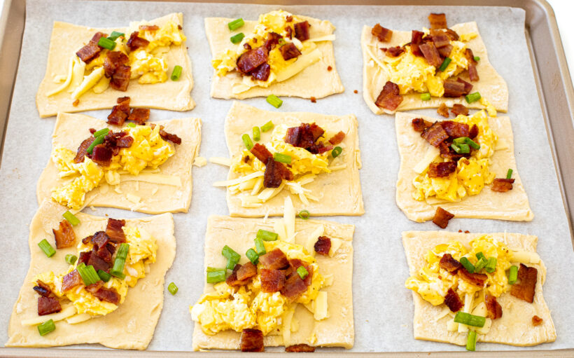 Puff pastry squares with toppings laid out on a baking sheet lined with parchment paper.