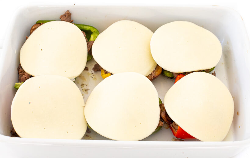 Stuffed Peppers with cheese slices on top in a white baking pan.