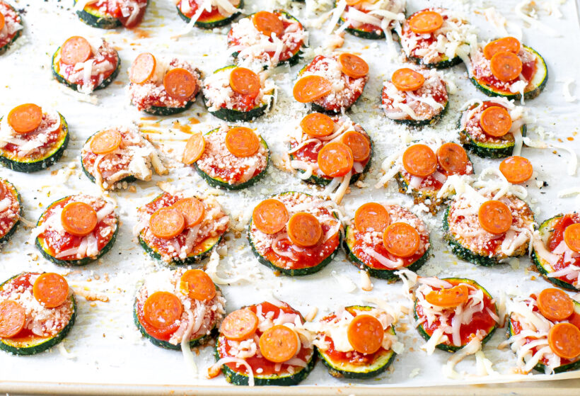 Mini pepperonis being placed on top of the slices of zucchini with cheese.