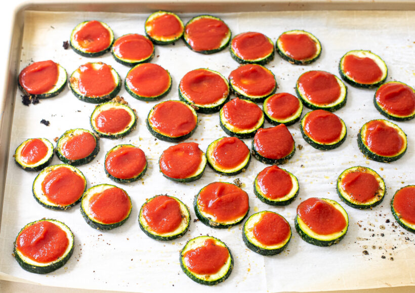 Zucchini slices topped with tomato sauce on a baking sheet.