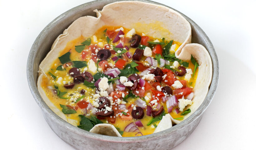 Toppings on top of the raw eggs on a tortilla in a cake pan.