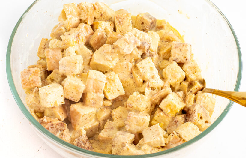 A spoon mixing the ingredients for eggnog casserole in a glass mixing bowl.