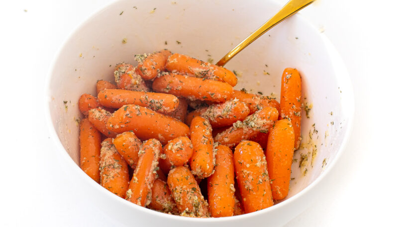 Carrots in a mixing bowl being coated in olive oil and ranch seasoning.