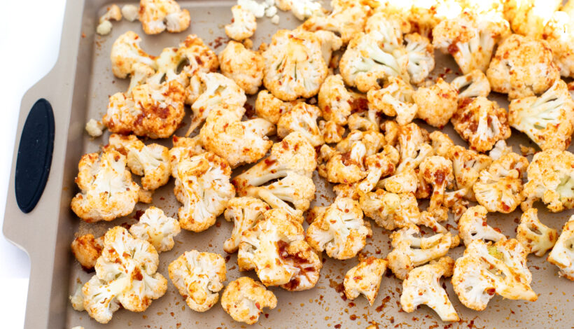 Pieces of cauliflower on a sheet pan coated in harissa paste before being baked.