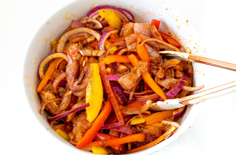 Mixing bowl with tossed fajita ingredients. Tongs are in the bowl.