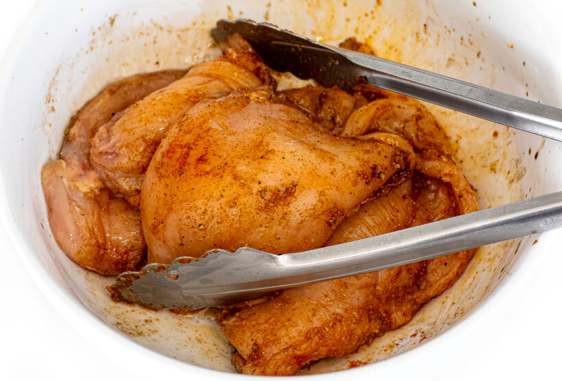 Chicken breasts marinating in a white mixing bowl.