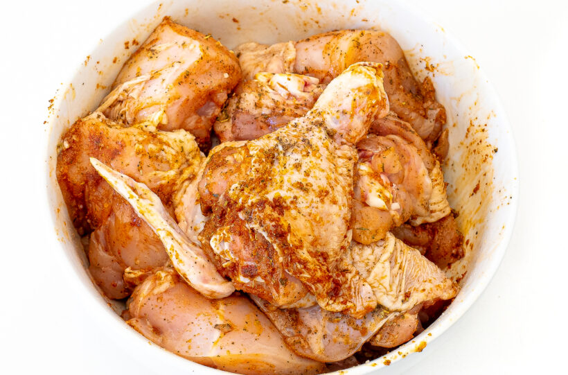 Pieces of chicken in a bowl covered in seasoning. 