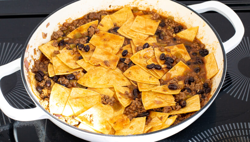 Mixture with beef and beans mixed with corn tortillas in a skillet. 