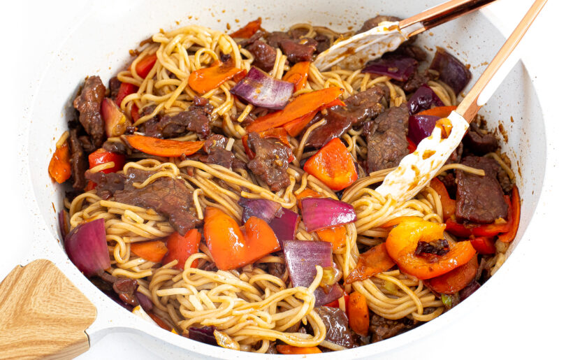 Steak, vegetables, and noodles tossed in a skillet.