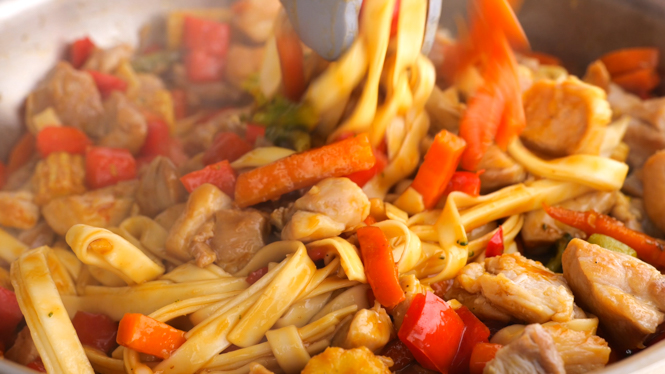 tossing noodles, chicken and vegetables in sauce