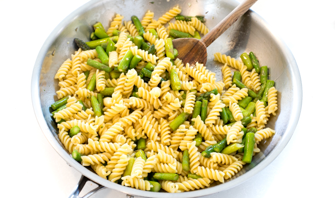 tossing cooked rotini with the cooked asparagus in skillet