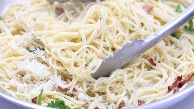 tossing pasta in carbonara sauce in skillet 