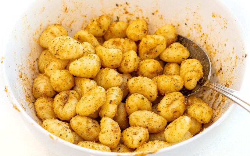 Gnocchi mixed with the seasonings and spices in a mixing bowl before being cooked.