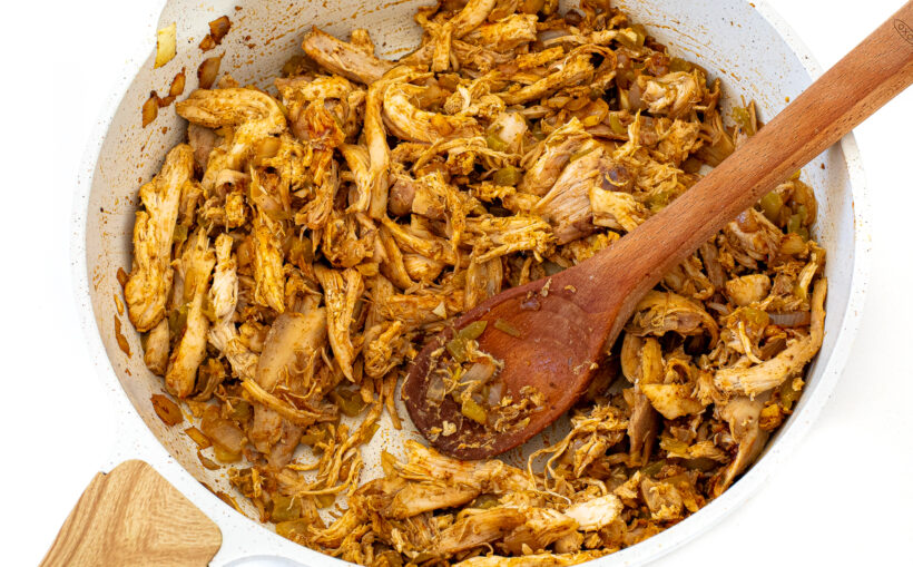 Shredded chicken added to the skillet with a wooden spoon stirring it.