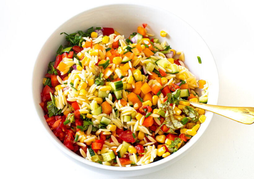 Orzo pasta salad being mixed with the homemade dressing. 