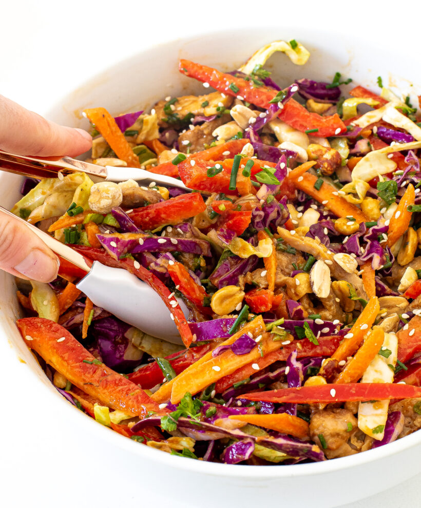 Hand holding tongs tossing a Thai chicken salad in a big bowl. 